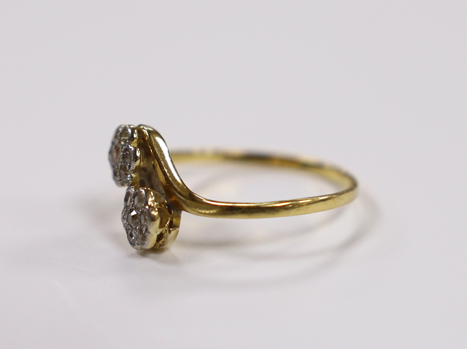 A yellow metal and diamond cluster set double flower head crossover ring, size N/O, gross weight 2 grams.